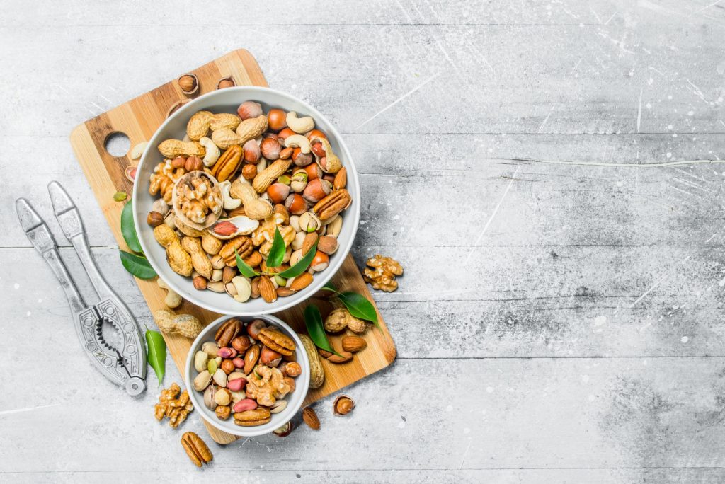 Different types of nuts in bowls with green leaves.